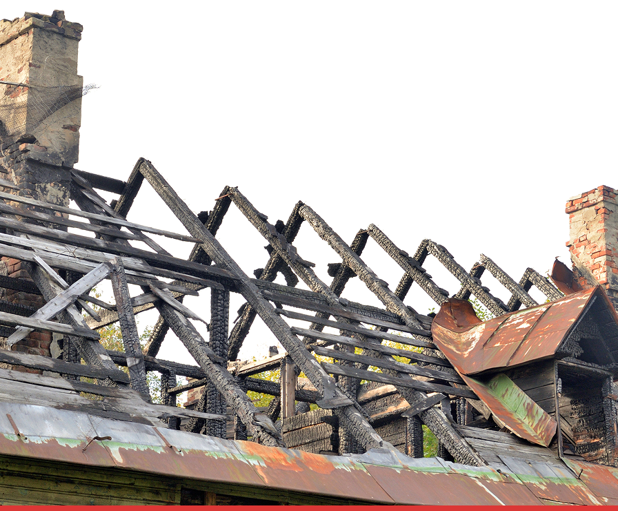 The image shows the charred remains of a building’s roof in Charlotte, with blackened wooden beams and damaged brick chimneys—an ideal project for Divine Restoration Group, experts in property restoration after fire damage. The metal roofing is rusted and partially collapsed.